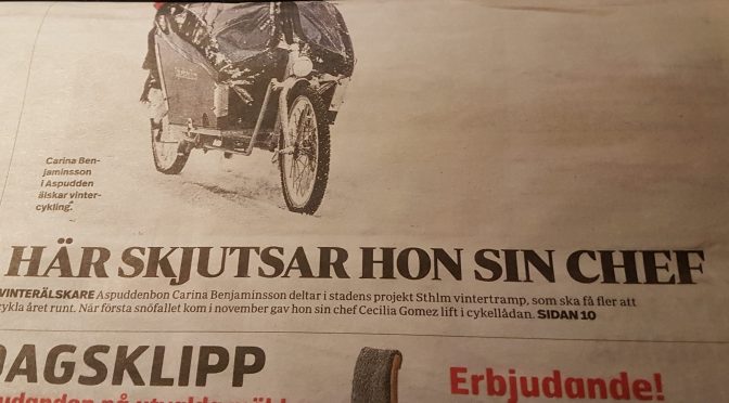 Dubbelvikt tidning med rubrik "Här skjutsar hon sin chef" under en halv bild. På bilden syns ett flerhjuligt fordon och nederkanten av ett regnplagg.